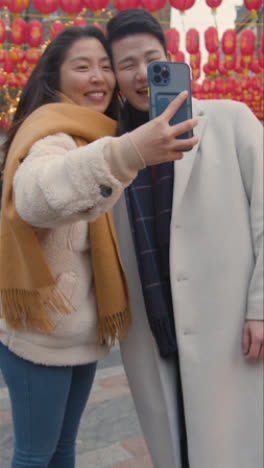 Video-Vertical-De-Una-Joven-Pareja-Asiática-De-Vacaciones-Posando-Para-Una-Selfie-En-Un-Teléfono-Móvil-En-Chinatown,-Londres,-Reino-Unido-2